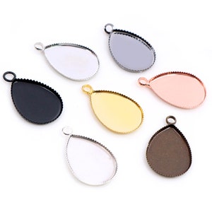 Puede incluir: Una colección de bandejas colgantes en forma de lágrima en varios acabados metálicos, incluyendo plata, negro, dorado y oro rosa. Cada bandeja tiene un borde festoneado y un pequeño lazo para sujetar una cadena o cordón, ideal para bisutería.