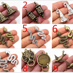 May include: Nine different charm pendants in silver and bronze finishes. The charms include a witch's hat, a lantern, a snake, a wolf's head, a Final Fantasy Adventure logo, and a bird.