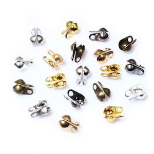 Pode incluir: Conjunto de tampas de contas metálicas em tons dourados, prateados e bronze. Cada tampa tem uma pequena bola na parte superior e dois laços nas laterais para prender às joias.