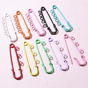 May include: Assortment of colourful safety pins with multiple loops. The pins are in various colours, including red, orange, yellow, green, blue, purple, and white.