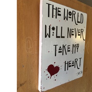 May include: White wooden sign with black text that reads "The World Will Never Take My Heart - MCR". A red heart with blood splatter is below the text.