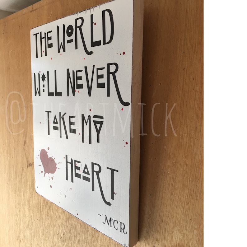 May include: White wooden sign with black text that reads "The World Will Never Take My Heart - MCR". The sign has a red heart shape with red splatters around it.