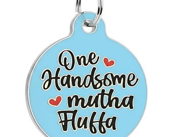 May include: A round, light blue metal pet ID tag featuring a silver-toned border and a silver split ring at the top. The tag displays the black text "One Handsome mutha Huffa" in a stylised font, accented by two small, solid red heart icons.