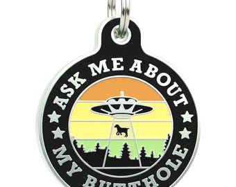May include: A black and silver pet tag with the text "ASK ME ABOUT MY BUTTHOLE". The tag features a colorful graphic of a UFO, a dog silhouette, and a forest scene.