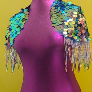 May include: A sequined shoulder wrap with a fringe trim. The sequins are iridescent and have a green, blue, and gold colour scheme.