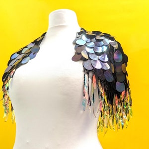 May include: A black sequined shoulder piece with iridescent sequins and fringe. The fringe is a mix of black, gold, and iridescent colours.