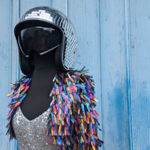 May include: A silver disco ball helmet with a black visor, worn with a silver sequined top and a colourful fringe vest.