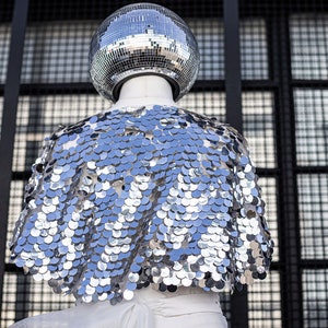 May include: A silver sequined cape with a disco ball on top of a mannequin.