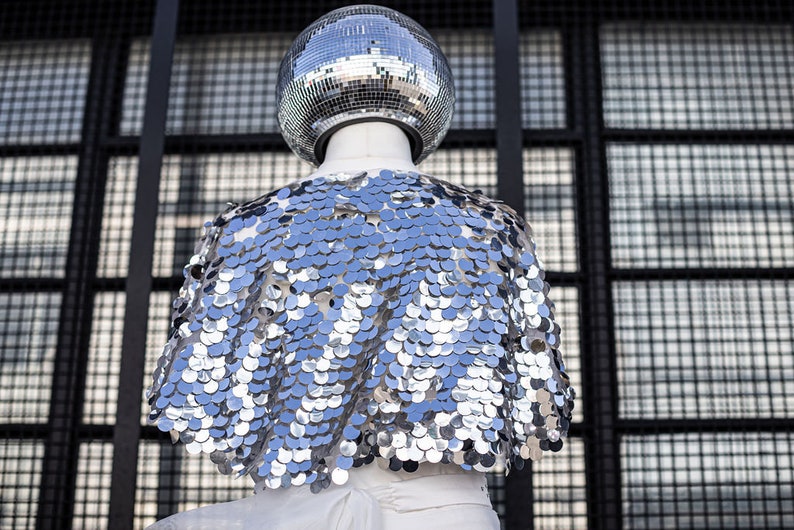May include: A silver sequined cape with a disco ball on top of a mannequin.