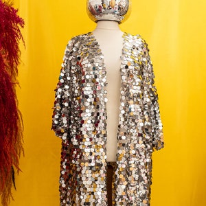 May include: A silver sequined kimono with a disco ball head on a mannequin against a yellow background.