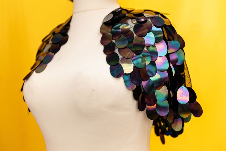 May include: A black mesh shrug with iridescent sequins in a circular pattern. The sequins are arranged in a cascading design, creating a dramatic and eye-catching look.