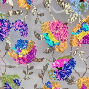 May include: A white sheer fabric with colourful sequins sewn in a floral pattern. The sequins are in shades of pink, blue, yellow, and green.