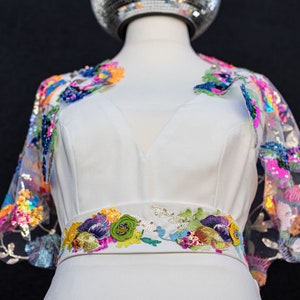 May include: A white dress with a colourful floral embroidered belt and matching floral embroidered sleeves. The sleeves are sheer and have sequins.