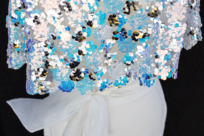 May include: White dress with a blue and silver sequined top. The top has a bow tie at the waist.