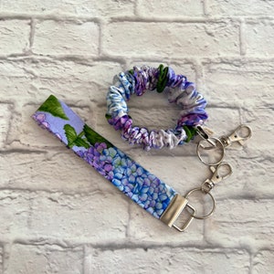 Könnte beinhalten: Ein lila-grüner Scrunchie mit Blumenmuster und ein passender Schlüsselanhänger mit einem silbernen Schlüsselring.