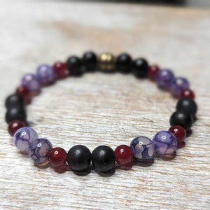 May include: A beaded bracelet with black, purple, and red beads. The bracelet has a gold clasp.