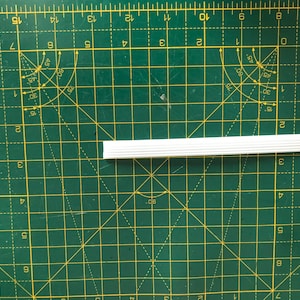 May include: A white plastic trim piece with a ribbed texture. The trim is about 10 inches long and is lying on a green cutting mat.