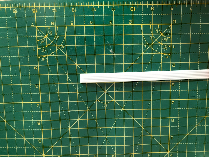 May include: A white plastic trim piece with a ribbed texture. The trim is about 10 inches long and is lying on a green cutting mat.