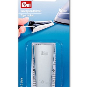 Può includere: Un attrezzo per creare il bias in plastica bianca con il nome del marchio "Fym" stampato su di esso. L'attrezzo per il bias è largo 18 mm ed è confezionato in una scatola di cartone blu e bianca. La scatola ha il testo "Schrägbandformer" e "Tape maker" stampato su di essa.