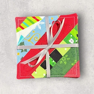 Pode incluir: Um conjunto de quatro bases quadradas de tecido com um design de patchwork. As bases apresentam padrões vermelhos, verdes, azuis e brancos, amarradas com uma fita prateada. O design inclui listras diagonais e motivos festivos.