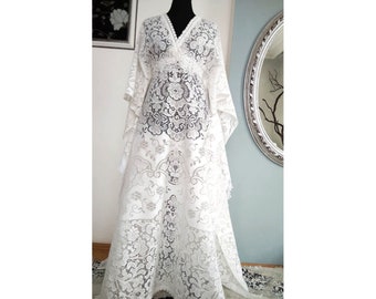 Könnte beinhalten: Ein weißes Maxikleid aus Spitze mit V-Ausschnitt und langen Ärmeln. Das Kleid hat einen fließenden, Boho-Stil.