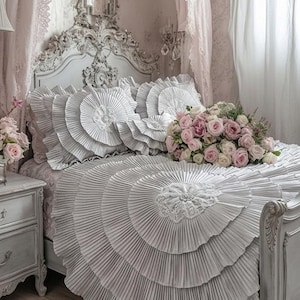 Può includere: Una lussuosa camera da letto con un letto con copriletto e cuscini grigi a pieghe. Un bouquet di rose rosa è appoggiato sul letto. La stanza comprende un lampadario, un comodino e un tappeto floreale.