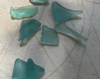 May include: A collection of seven sea glass pieces in various shapes and sizes. The glass is a light blue color and has a translucent appearance.