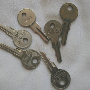 May include: A collection of five silver keys with the word "GAS" printed on four of the keys.