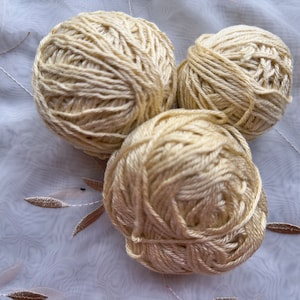 Puede incluir: Tres ovillos de hilo de color crema, probablemente para tejer o hacer ganchillo.