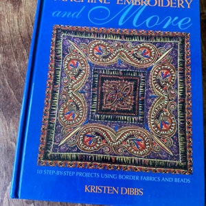 May include: A blue book titled "MACHINE EMBROIDERY and More" with a colorful paisley design. The book cover includes the text "10 STEP-BY-STEP PROJECTS USING BORDER FABRICS AND BEADS" and the author's name, "KRISTEN DIBBS."
