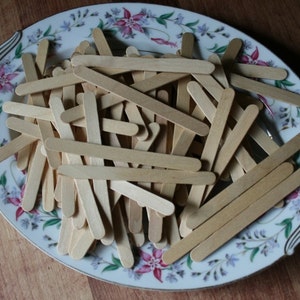 Puede incluir: Un plato ovalado de cer&aacute;mica blanca con un dise&ntilde;o floral presenta una pila de palitos de madera.