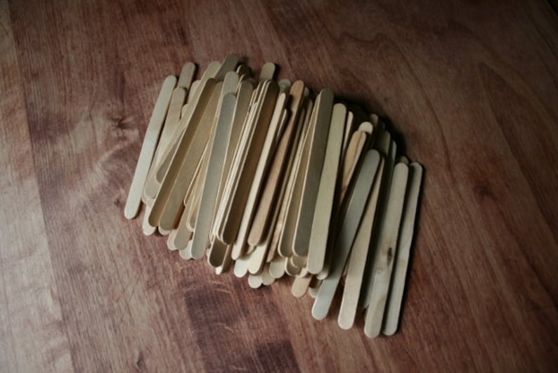 Puede incluir: Un mont&oacute;n de palitos de manualidades de madera natural, dispuestos en un patr&oacute;n suelto y superpuesto sobre una superficie de madera marr&oacute;n.