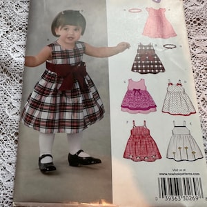 Puede incluir: Un patrón de costura para vestidos de bebé. El patrón incluye cinco estilos diferentes de vestidos, incluyendo un vestido de cuadros, un vestido rosa con un lazo, un vestido blanco con lunares, un vestido rojo de cuadros vichy y un vestido blanco con flores. El patrón es de New Look y es talla NB-L.