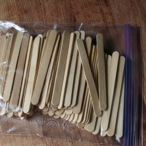 Puede incluir: Una bolsa de pl&aacute;stico transparente llena de una gran cantidad de palitos de manualidades de madera natural. Los palitos miden aproximadamente 10 cm de largo y tienen extremos redondeados.