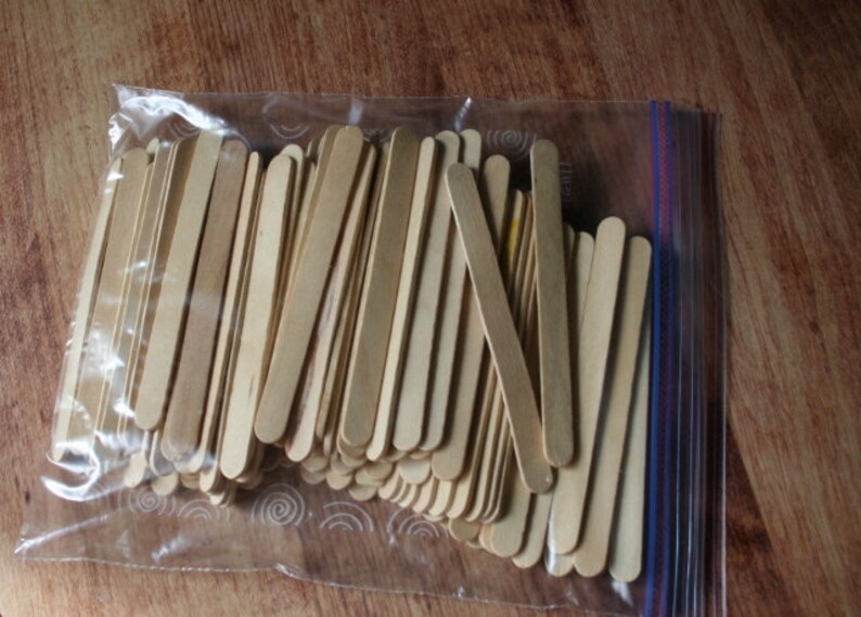 Puede incluir: Una bolsa de pl&aacute;stico transparente llena de una gran cantidad de palitos de manualidades de madera natural. Los palitos miden aproximadamente 10 cm de largo y tienen extremos redondeados.