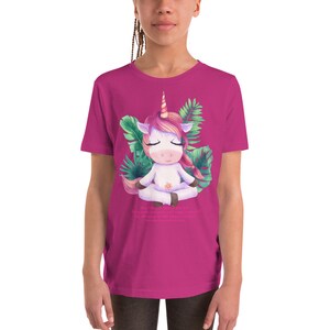 May include: A pink youth t-shirt with a white unicorn meditating in a green tropical leaf design. The text "I am a unicorn, I am magical, I am strong, I am beautiful, I am everything I want to be, I am magic" is printed on the shirt.