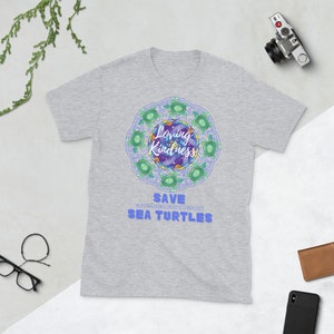 May include: A gray t-shirt with a blue and green mandala design featuring sea turtles. The mandala has the words "Loving Kindness" in the center. The text "Save Sea Turtles" is below the mandala with the hashtag "#spreadingkindnessmeditationeveryday".