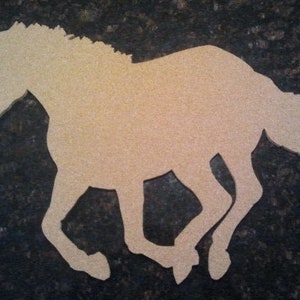 May include: A cutout of a horse running, made of light brown wood. The horse is facing left and has a long mane and tail.
