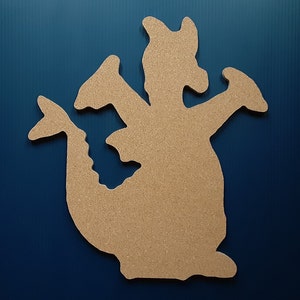 May include: A corkboard cutout of a dragon with a brown color. The dragon is facing the right side of the image and has its wings spread out. The dragon is on a blue background.