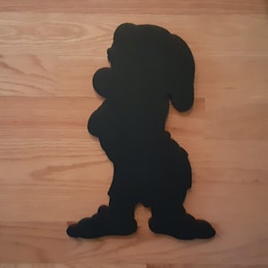 May include: Black silhouette of a cartoon dwarf with a pointed hat, standing with one leg slightly bent and arms crossed.