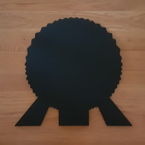 May include: A black, circular award with a scalloped edge and a ribbon attached. The award is made of a solid material and has a matte finish.