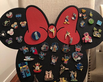 May include: A black foam Mickey Mouse head with a red bow, covered in various Disney character pins. The pins feature characters like Stitch, Tinkerbell, and Mickey Mouse.