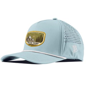 May include: A light blue baseball cap with a white rope detail across the brim. The front features an olive green patch with a mountain and pine tree graphic, the text PEAK PERF, and EST. 2000. The side panel has laser-cut ventilation holes.