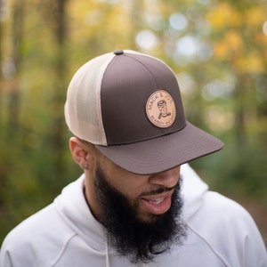 May include: A brown and beige trucker hat with a brown leather patch that says "Mack & Jo's Beanery and Bakery".