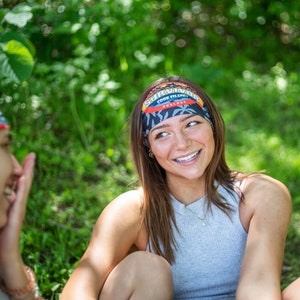 K&ouml;nnte beinhalten: Zwei Personen tragen Stirnb&auml;nder mit dem Text "Survivor Cook Islands" und einem tropischen Design. Die Stirnb&auml;nder sind schwarz, rot und blau. Eine Person tr&auml;gt ein graues Tanktop und l&auml;chelt. Der Hintergrund ist gr&uuml;n.