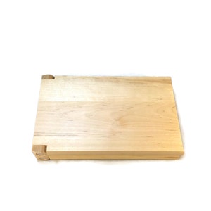 May include: A natural wood chopping board with a hinged design. The board is made of light wood with a smooth surface.