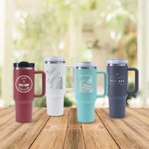 May include: Four stainless steel travel mugs with different designs and colours. The mugs have a black lid and a handle. The designs include a mermaid, a wedding couple, a camp counsellor logo, and the words "Best Man".