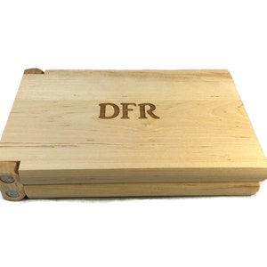 May include: A wooden box with a hinged lid, made of light wood with a natural finish. The box is engraved with the initials "DFR".