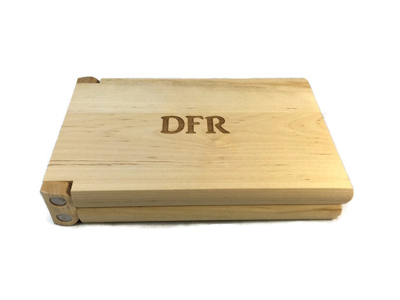 May include: A wooden box with a hinged lid, made of light wood with a natural finish. The box is engraved with the initials "DFR".