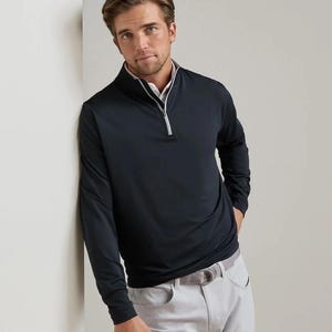 May include: A long-sleeve navy blue pullover with a quarter-zip closure featuring a light gray inner lining and trim. The garment is paired with light gray trousers that have a visible belt loop and a silver-toned buckle at the waistline.